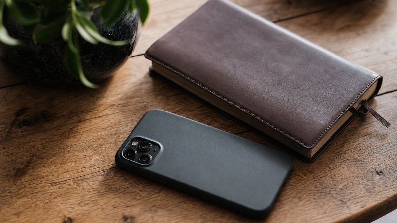 An iPhone face-down beside a closed leather notebook on a wooden table